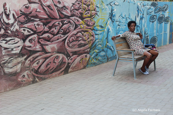 woman on bench surrounded by mural art